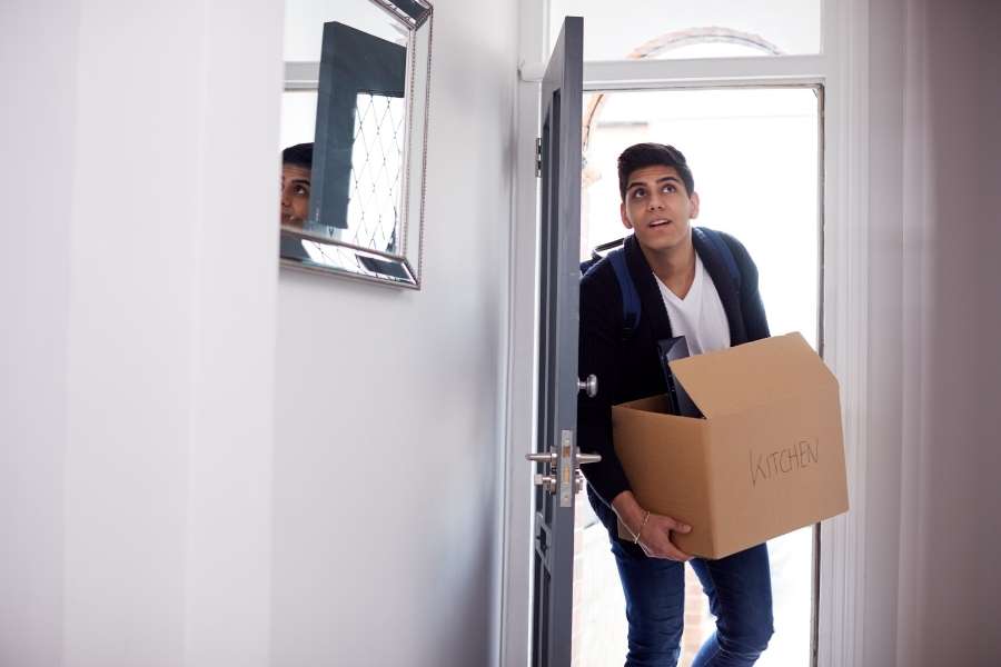 Un jeune homme arrive dans son nouveau logement avec un carton, une étape décisive pour réussir une colocation rentable.