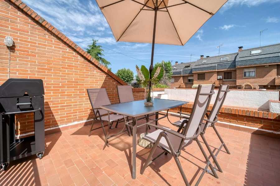 Un parasol beige ouvert sur une terrasse en briques permet d'ombrager un petit balcon aménagé pour les repas.