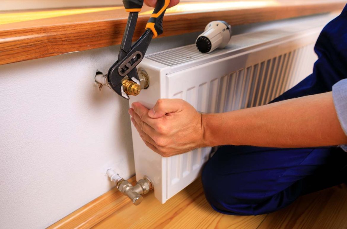 Un professionnel en bleu utilise une pince pour intervenir sur l'installation afin de purger circuit plomberie et radiateur