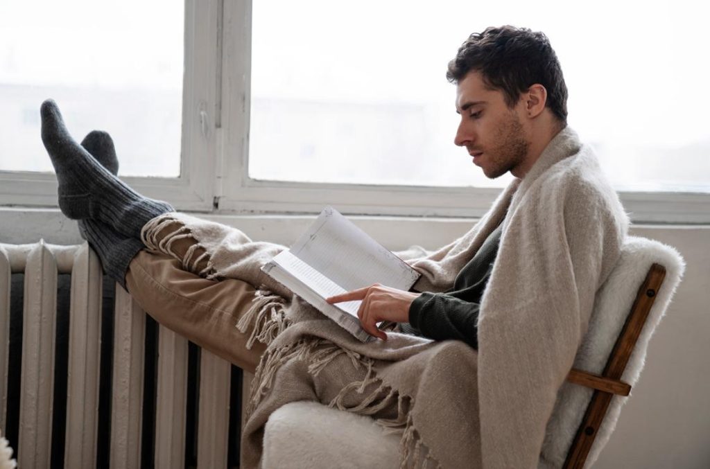 Un homme confortablement installé dans un fauteuil près d'un radiateur, illustrant le fonctionnement chauffage accumulation en hiver.